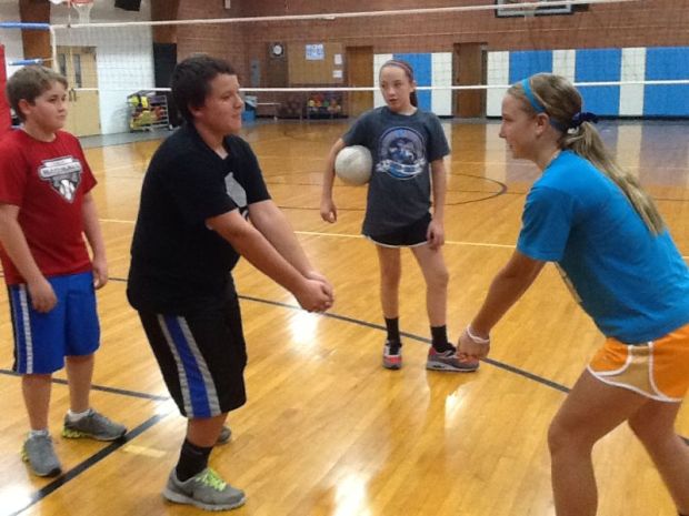 Coach Julie Martin demonstrates proper technique in passing a volleyball to her teammates Noah Newcomb and Kyler Sphan, while coach Torie Thomas looks on.