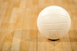 A lone white volleyball sitting on a wooden floor