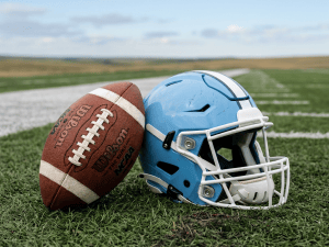 Football beside a light blue helmet on an empty stadium field