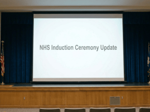 Students attend an NHS induction ceremony update in an auditorium